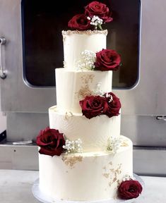 a three tiered cake with red roses on the top and white flowers on the bottom