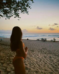 a woman standing on top of a sandy beach next to the ocean with people in the background