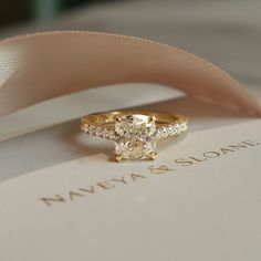 a diamond ring sitting on top of a white box with a pink ribbon around it