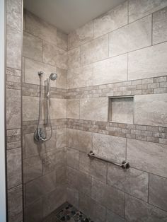 a walk in shower sitting next to a tiled wall and floor covered in gray tiles