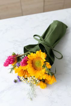 a bouquet of sunflowers and other flowers on a white tablecloth with a green bow