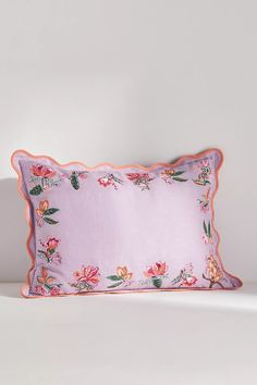 a pink pillow with flowers on it sitting on a white table next to a wall