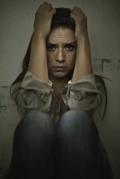 a woman sitting in front of a wall with her hands on her head