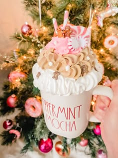 someone is holding up a cupcake in front of a christmas tree with ornaments on it