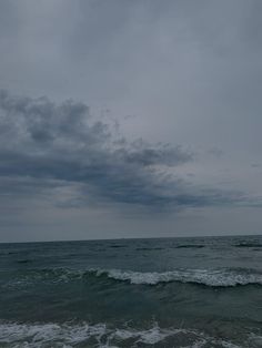 an ocean with waves crashing on the shore and dark clouds in the sky above it