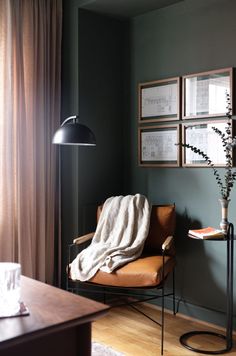 a chair with a blanket on it next to a lamp and pictures hanging on the wall