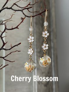 a pair of earrings with flowers hanging from it's earwires and the words cherry blossom written below them