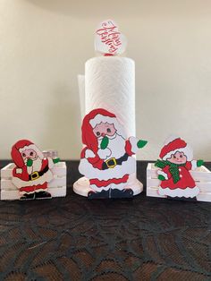 three santa clause toilet paper holders on top of a black table with a white wall in the background