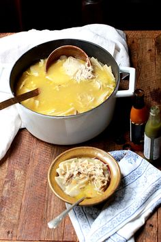 two bowls filled with soup sitting on top of a wooden table next to bottles and spoons