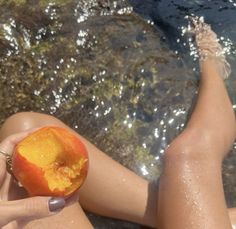 a woman holding an apple in her hand while sitting on the ground next to water