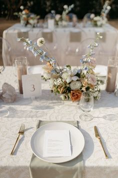 the table is set with white plates and silverware, napkins, and floral centerpieces