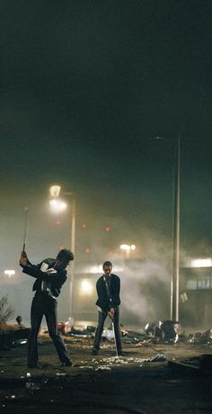 two men standing in the middle of a street at night with lights shining on them