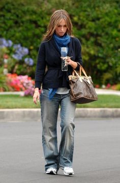 a woman is walking down the street with her cell phone in her hand and holding a purse