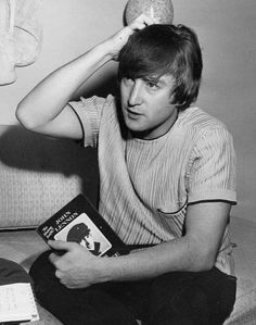 a young man sitting on a couch holding a book in front of his head and looking at the camera