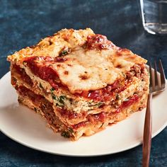 a stack of lasagna on a plate next to a fork and glass of water