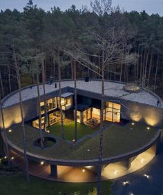 an aerial view of a circular house in the woods at night with lights on it