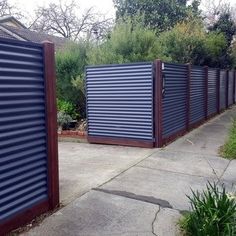 two metal gates on the side of a sidewalk next to grass and bushes in front of a house