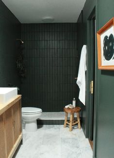 a white toilet sitting next to a wooden stool in a bathroom under a painting on the wall