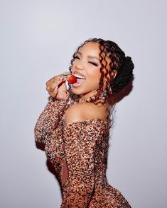 a woman with curly hair is smiling and holding a piece of fruit in her mouth