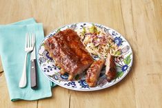 a plate with ribs and coleslaw on it next to a knife and fork