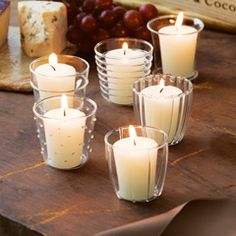 candles are sitting on a wooden table with cheese and grapes in the background