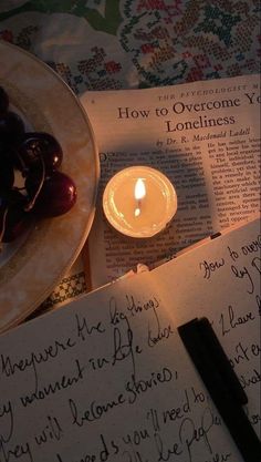 an open book with writing and a candle on it next to a plate full of cherries