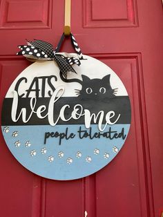 a sign that says cats welcome people to the cat's house and is hanging on a red door