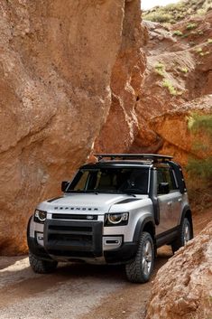 a silver land rover parked in front of a large rock