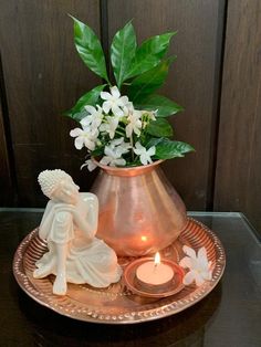 a vase filled with white flowers next to a lit candle on a tray near a wall