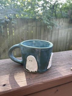 a cup with a ghost on it sitting on a wooden table next to a fence