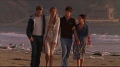 four people are standing on the beach with seagulls in the water behind them