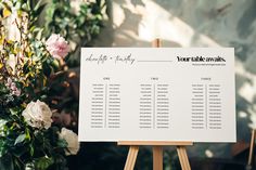 a white table plan sitting on top of a wooden easel next to some flowers