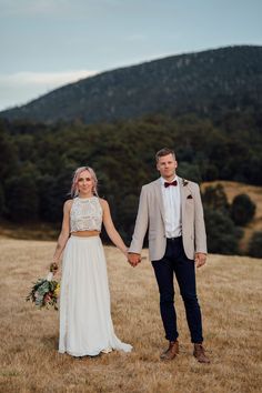 a bride and groom holding hands in a field with mountains in the background at their wedding