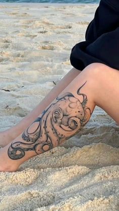 a person sitting in the sand with an octopus tattoo on their leg