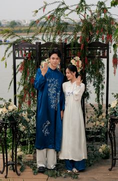 two people standing next to each other in front of flowers