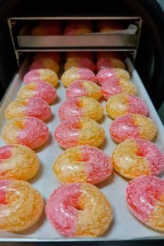 there are many pink and yellow donuts in the oven