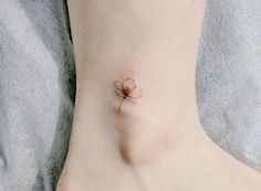 a small tattoo on the ankle of a woman's foot with a single flower