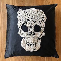 a black pillow with white lace and a skull on it's side sitting on a wooden floor