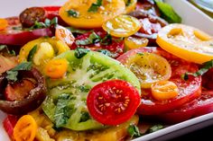 a white plate topped with lots of different types of tomatoes and cucumber slices