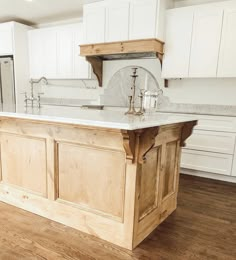 a large kitchen island in the middle of a wood floored room with white cabinets