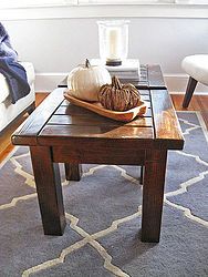 a coffee table with two pumpkins on it in front of a window and a blue rug