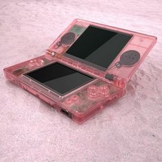 an open pink nintendo game console sitting on top of sand