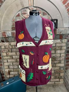 a mannequin wearing a sweater vest with pumpkins and leaves on it, in front of a brick wall