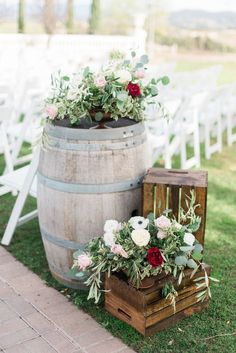 two wooden barrels with flowers and greenery on them are sitting in the grass next to each other