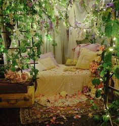 a bed covered in lots of flowers and greenery next to a canopy with lights