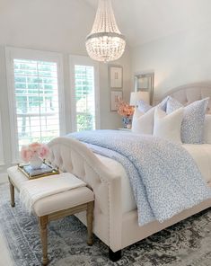 a white bed sitting in a bedroom next to a window with a chandelier