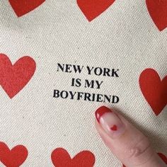 a woman's hand with red nail polish holding onto a new york is my boyfriend pillow