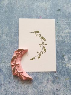 a card with a pink crescent and green leaves on it sitting on top of a blue surface