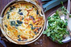 a quiche with cheese and spinach on a wooden table next to a salad