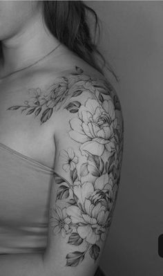 a woman's shoulder with flowers and leaves tattooed on her left arm, in black and white